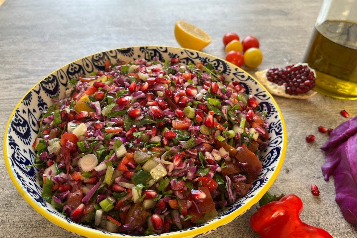 Een kleurrijke, fertig bereide granaatappelsalade in een decoratieve kom, geserveerd met een schijfje citroen en een fles olijfolie op de achtergrond
