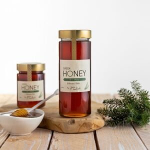 Een glazen pot Griekse honing van dennenboom met een houten lepel en een dennentakje op een houten tafel