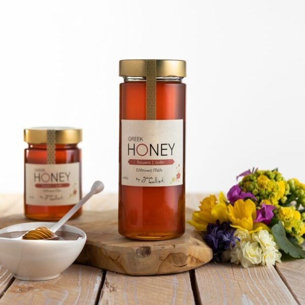 Een glazen pot met Griekse bloemenhoning, een witte kom met een honingdipper en een boeketje verse lentebloemen op een houten tafel