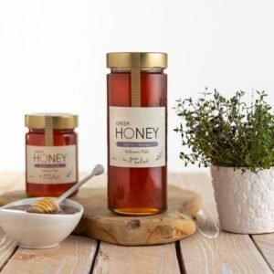 Een glazen pot met Griekse tijmhoning, vergezeld van een kom met een honingdipper en een pot verse tijmplant op een houten tafel