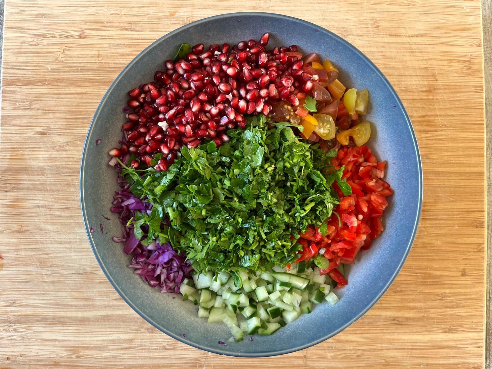 Een kleurrijke, ongeklede salade in een kom, zorgvuldig gerangschikt met gesneden granaatappelpitjes, rode kool, komkommer, paprika en verse peterselie