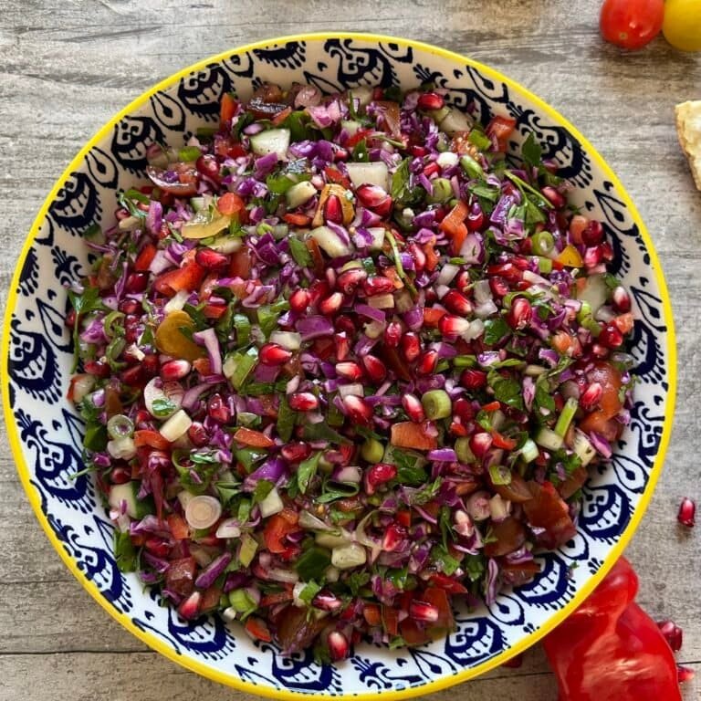 Kleurrijke Griekse salade met verse ingrediënten, waaronder ui, tomaat, paprika en peterselie in een blauw-wit patroon schaal.